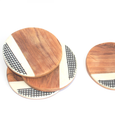 4 round handcrafted wood coasters that are brown in color. They are made from olive wood and recycled cow bone. The coasters have a brown smooth surface and a white marble looking inlay along the bottom edge of each coaster. The white inlay is made from recycled cow bone. The white recycled cowbone also has hand drawn black lines that cross each other horizontally and vertically.
